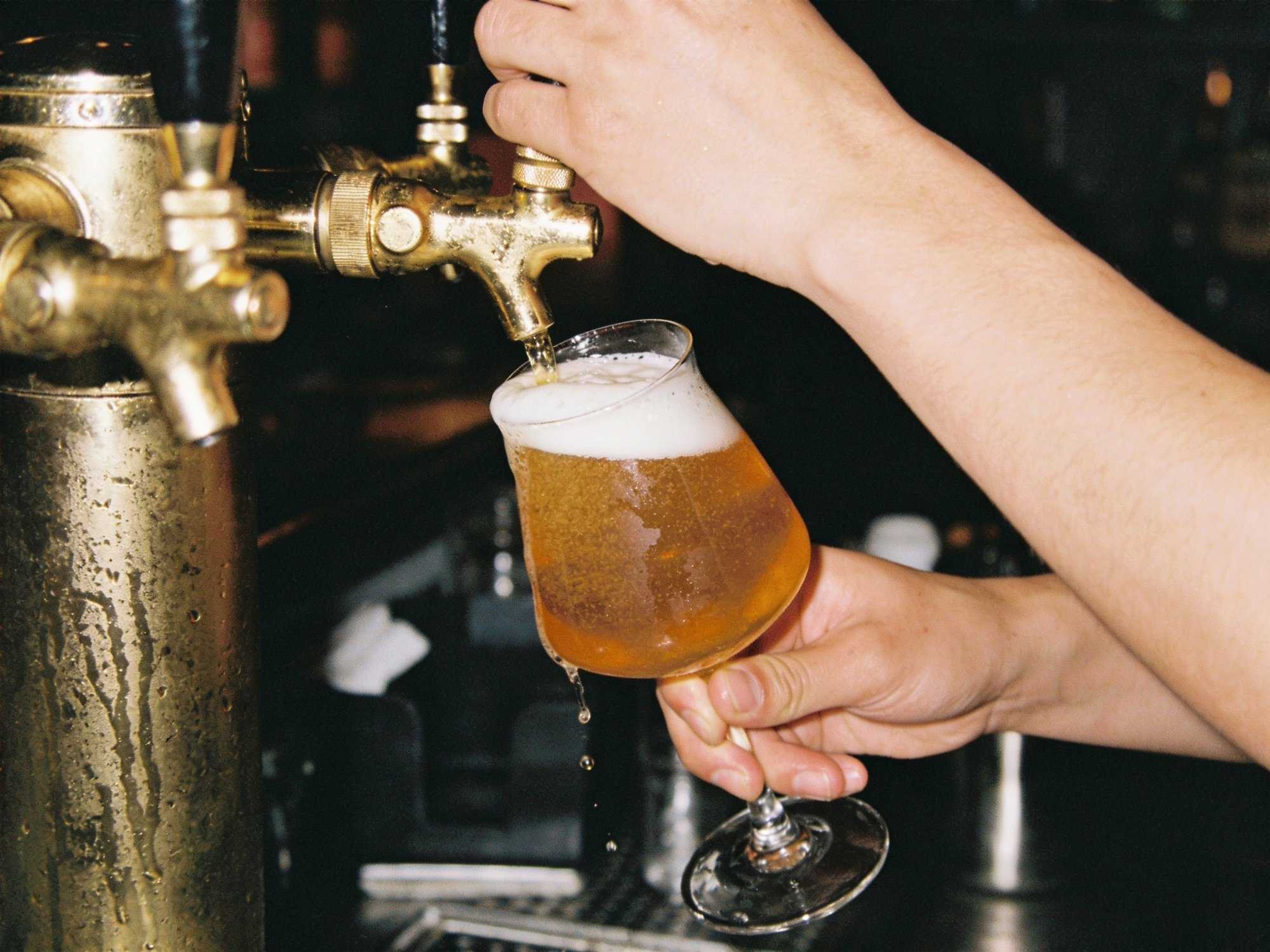 A bartender's hands pulling a brass tap, beer foaming into a tulip glass